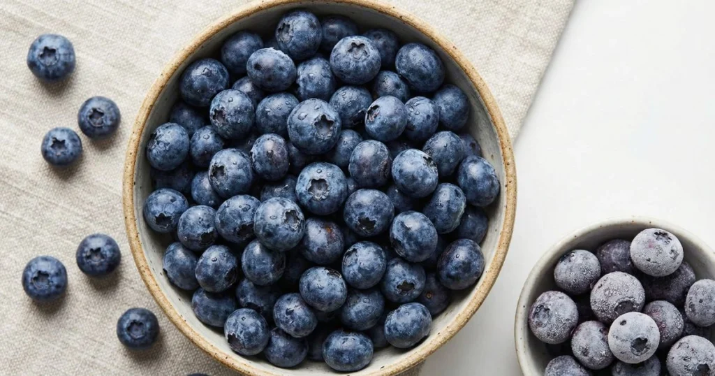 fresh blueberries in a rustic bowl with a few scattered loose berries, deep blue and purple tones.